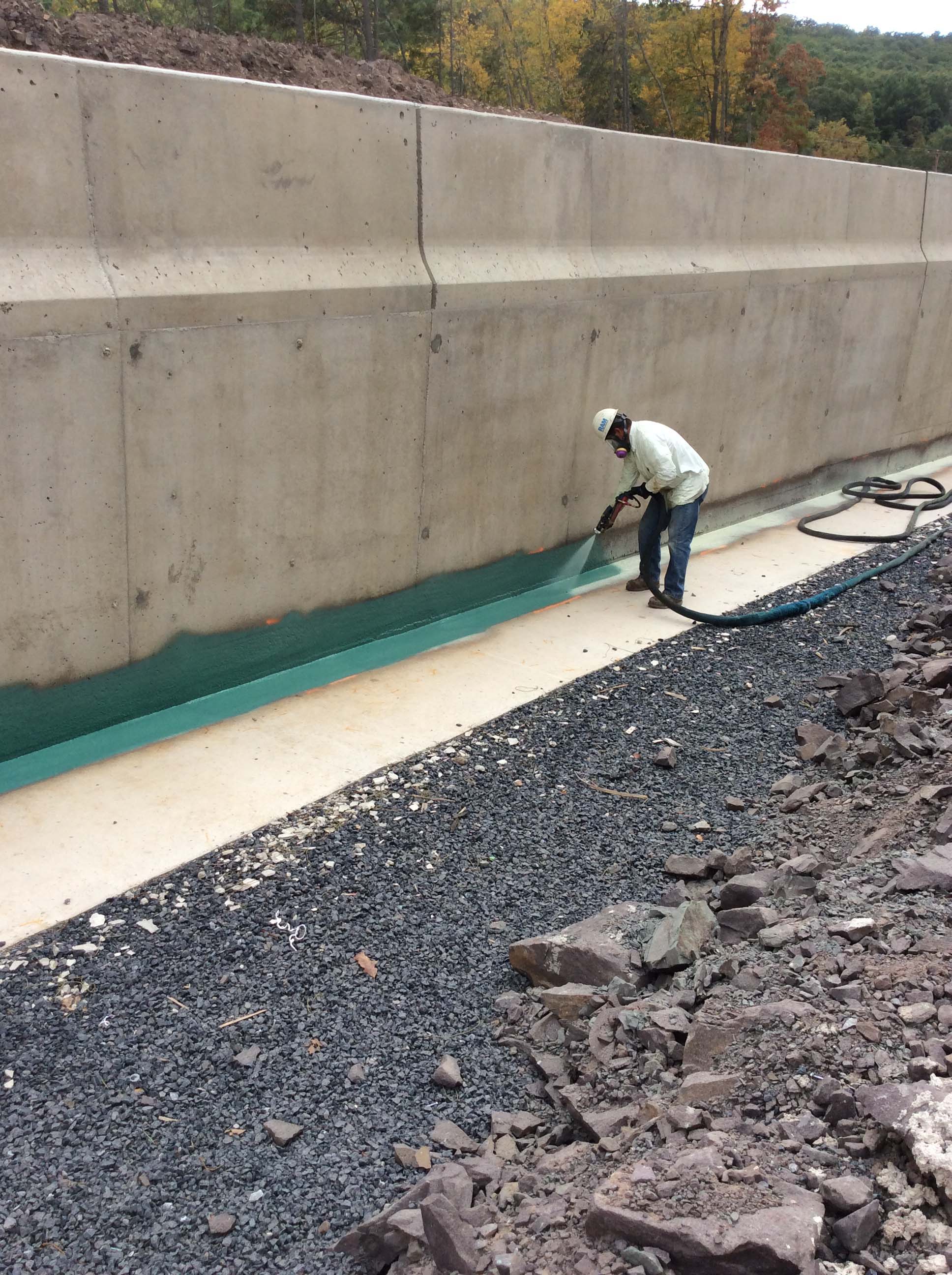 An image of a construction worker using a sprayer to apply a green coating to a bridge.